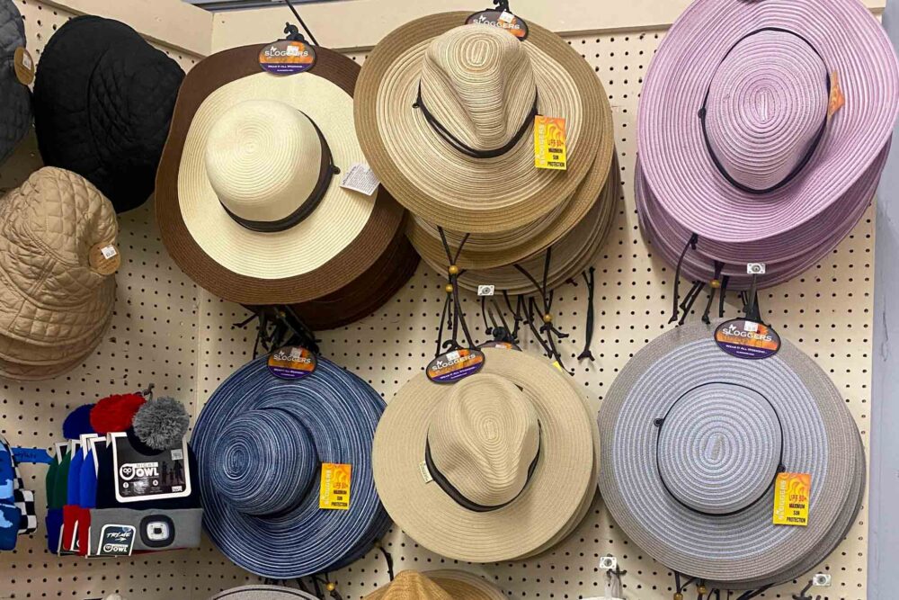 Various hats displayed on a pegboard, including straw and quilted styles in different colors.