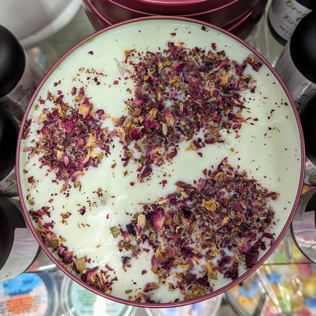 A round candle with a pale green surface topped with dried rose petals.