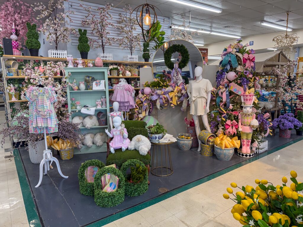 A store display featuring pastel children’s clothes, seasonal holiday decor, Easter accents, and baskets arranged on shelves in Baton Rouge.