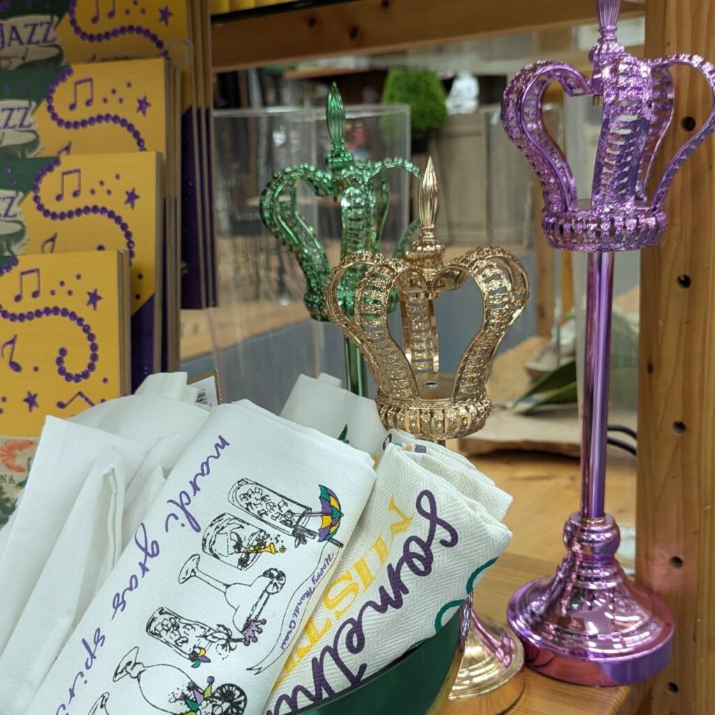 Three metallic crown decorations in green, gold, and purple bring seasonal holiday decor to a Baton Rouge wooden shelf with festive napkins.