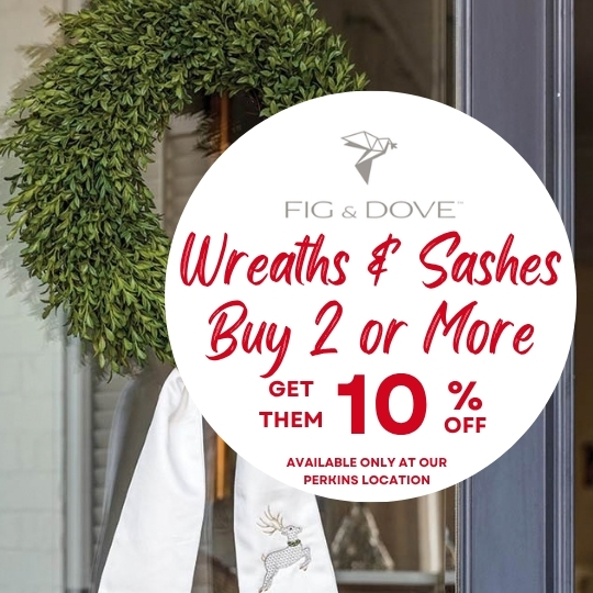 A green wreath with a white sash hangs on a door. Text on a circle advertises a buy 2 or more, get 10% off sale at Fig & Dove.