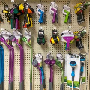 A display of various colorful garden hose nozzles and watering tools on a pegboard.